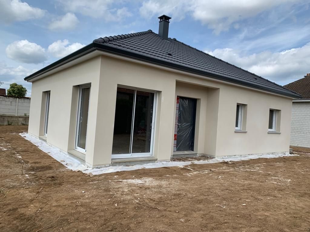 Une maison blanche avec un toit noir se trouve au milieu d'un champ de terre.